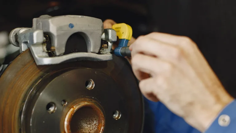 Mechanic measuring a brake rotor with a micrometer next to the brake caliper on a car