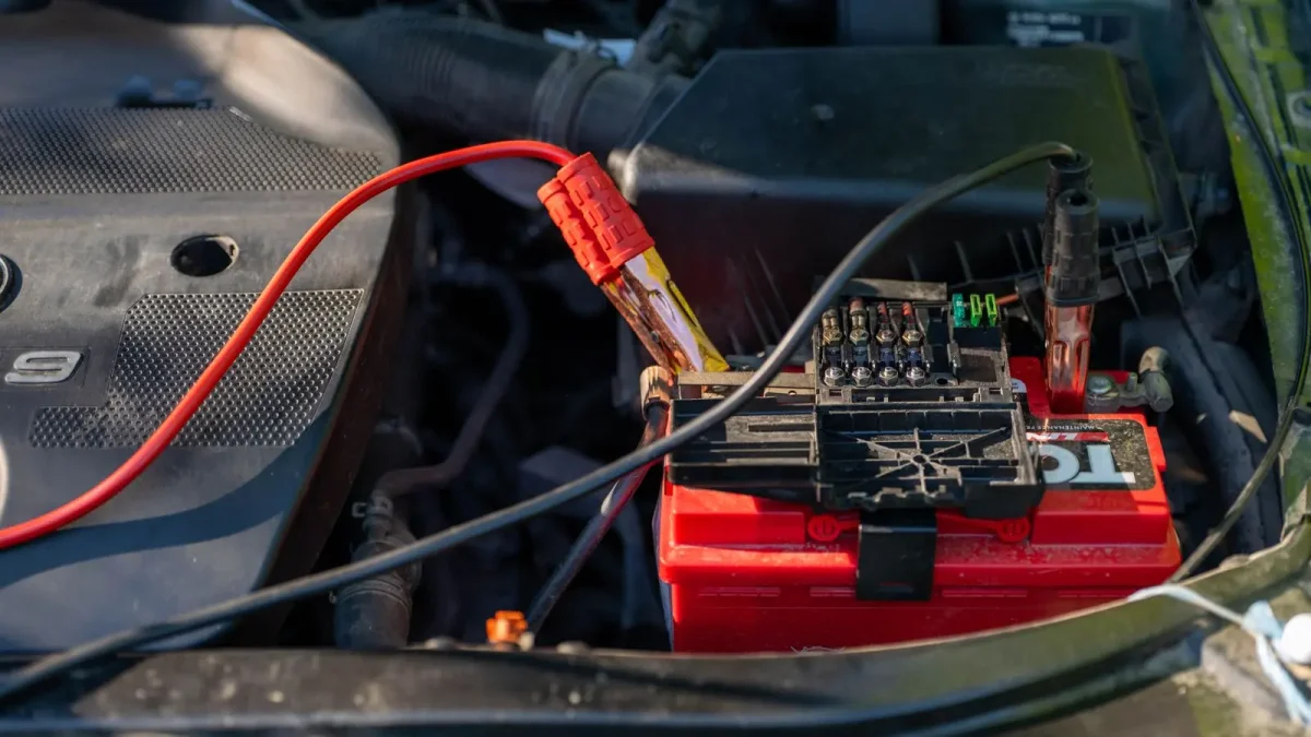 Red car battery in an engine bay with jumper cables attached