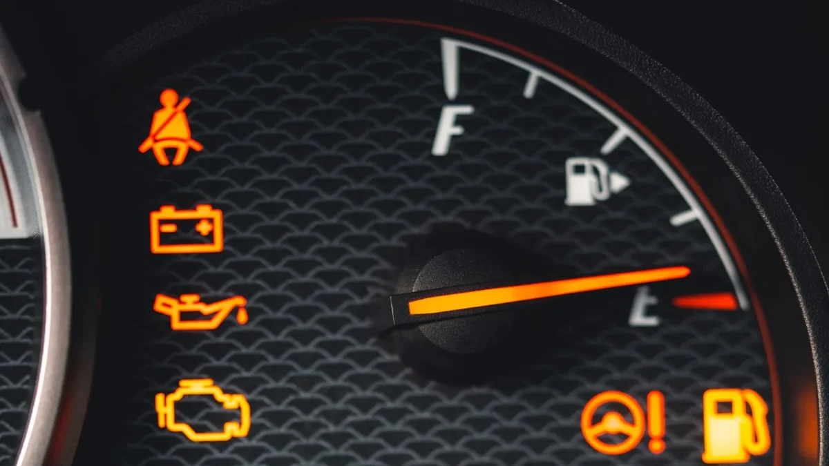Car dashboard gauge cluster with the orange check engine warning light illuminated