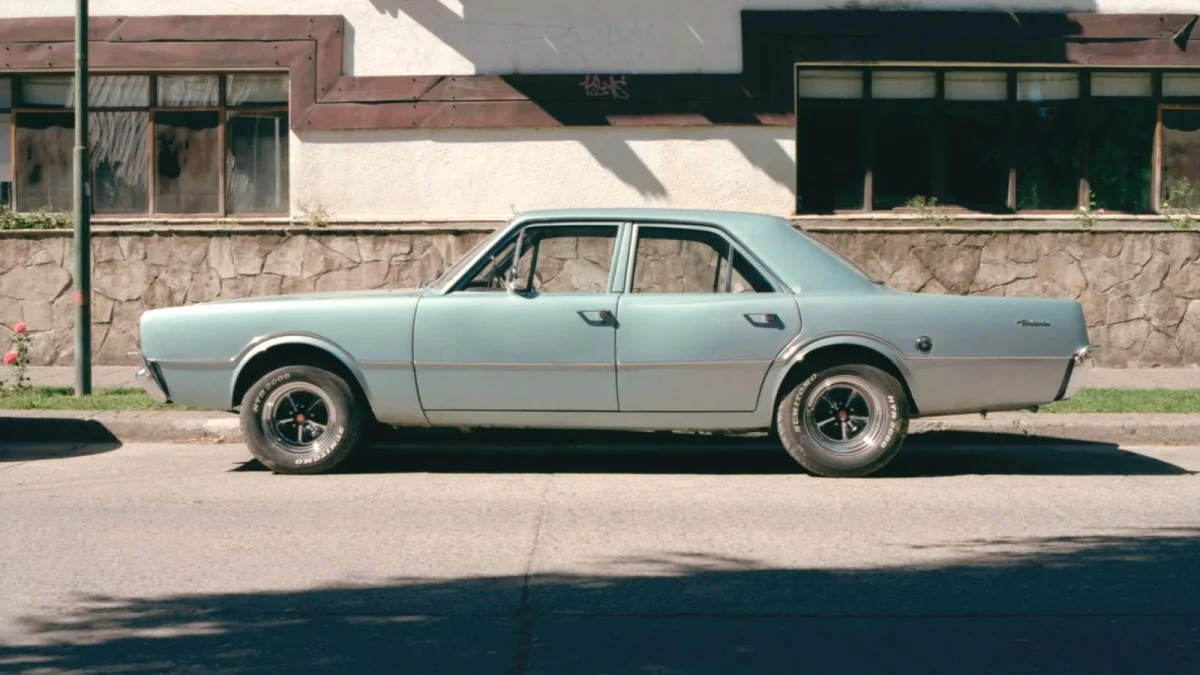 Older blue four-door sedan parked at the curb in front of a stone wall