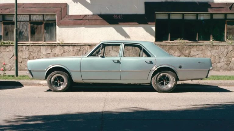 Older blue four-door sedan parked at the curb in front of a stone wall