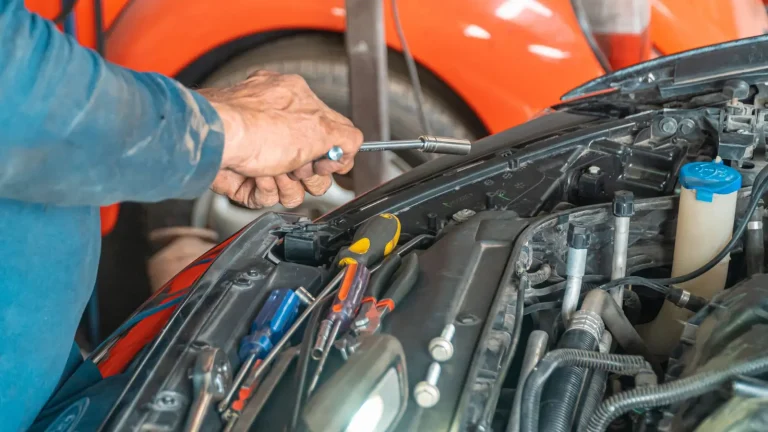 Mechanic using a wrench on a car engine under the open hood in a garage