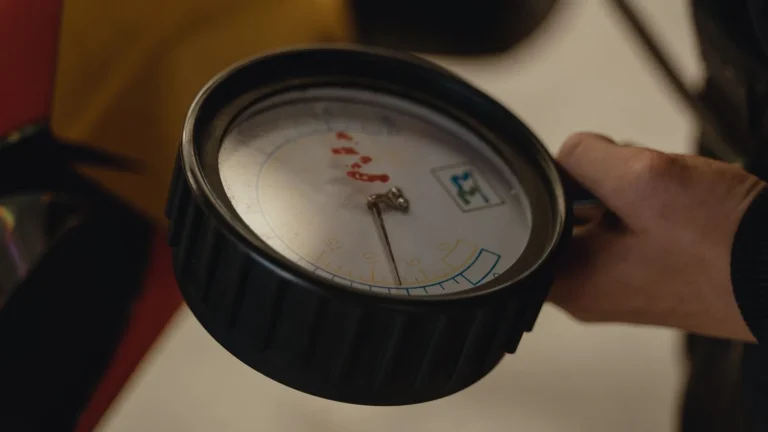 Hand holding an analog tire pressure gauge next to a car wheel
