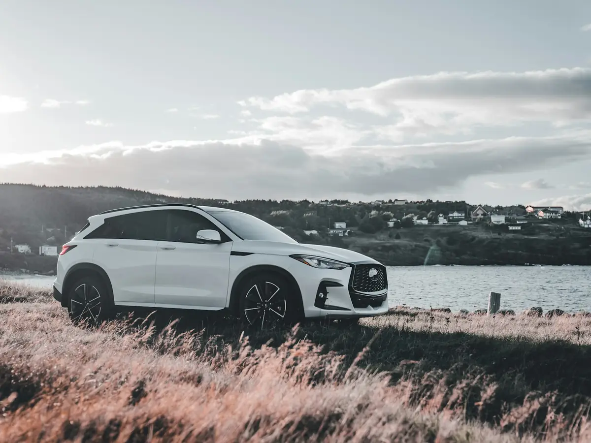 White compact SUV parked on a grassy shoreline beside a calm bay