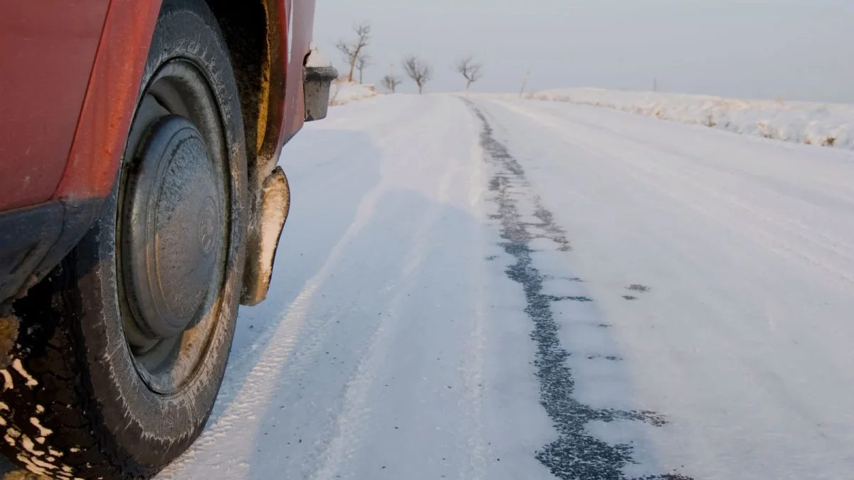Car tire beside a snow-covered winter road with tire tracks