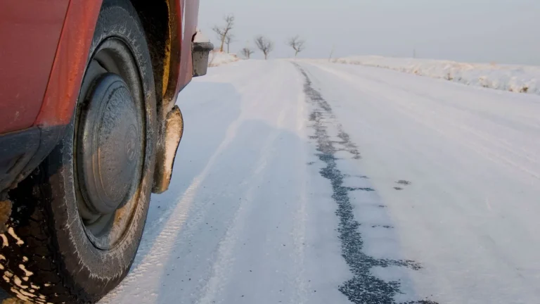 Car tire beside a snow-covered winter road with tire tracks